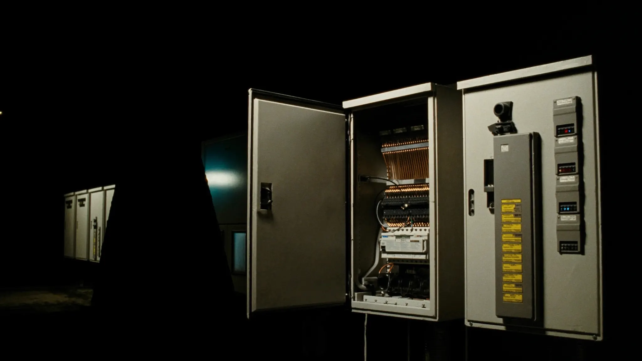 A lineup of medium-voltage switchgear cubicles in a substation at night, one door open on copper busbar and protective relays.