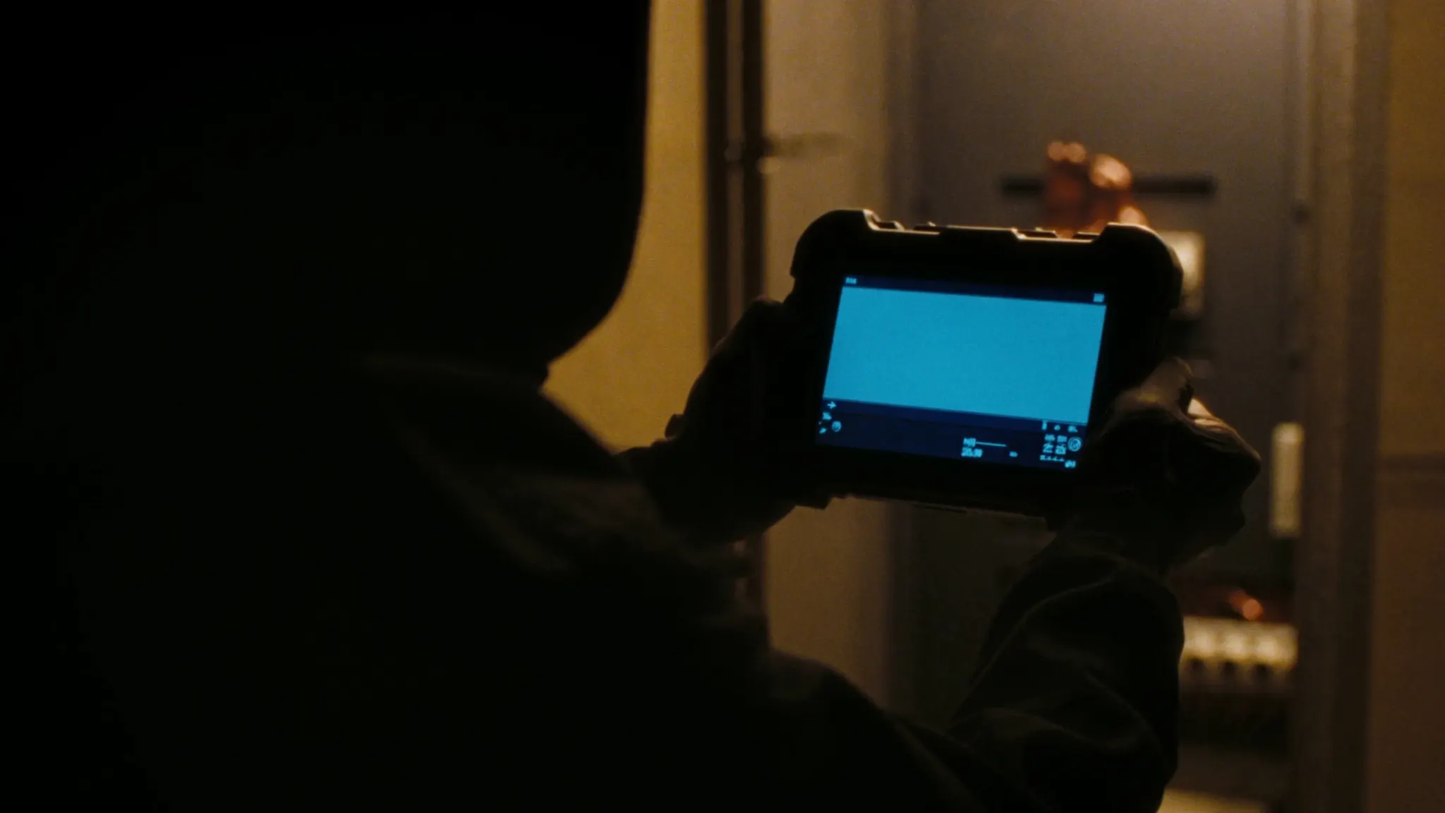 Gloved hands holding a rugged tablet up in front of an open switchgear cubicle, the screen lighting the gloves and cabinet edge.