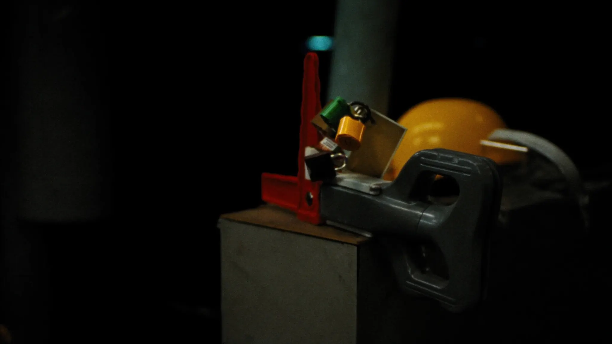 A disconnect switch handle clamped in a red lockout hasp carrying several padlocks and tags, hard hat and face shield resting behind it.